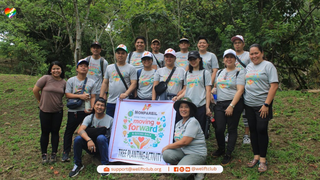 Nonpareil International team with We Lift Club at tree planting activity holding Moving Forward and Giving Back banner